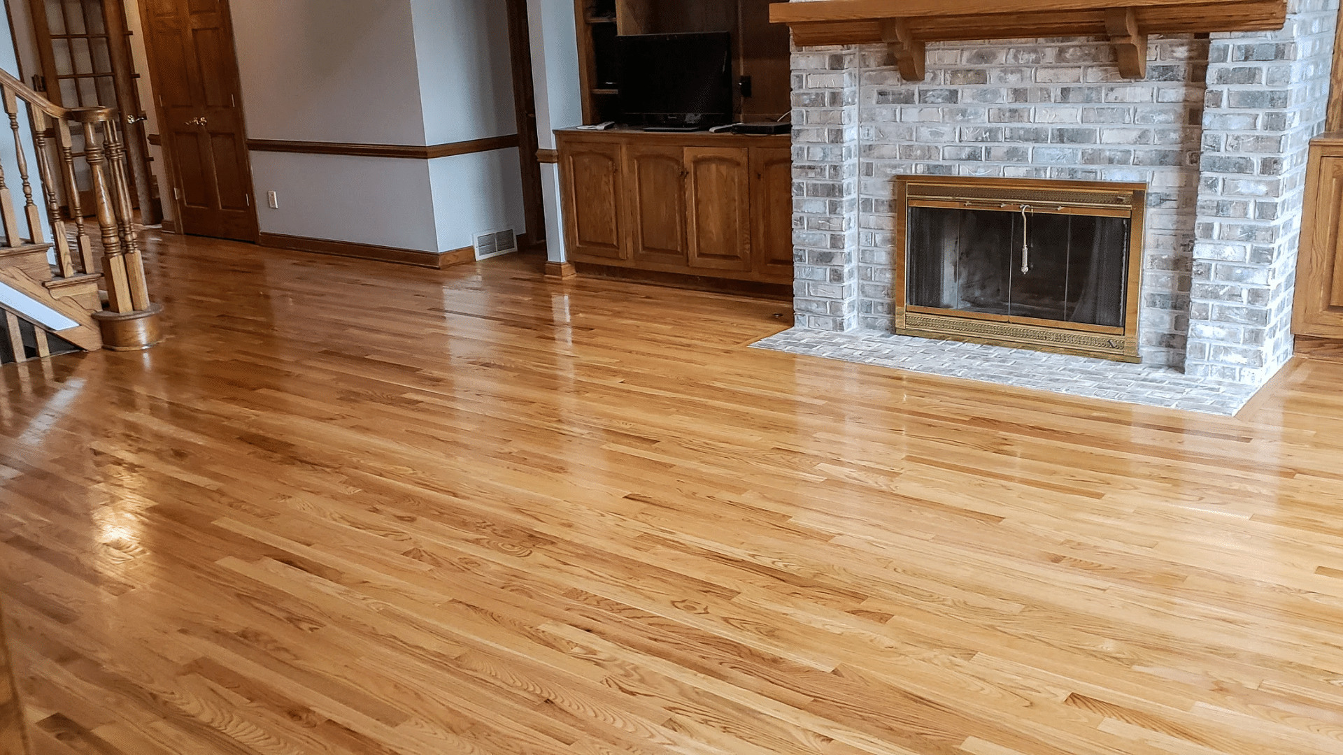 polished maple flooring across a living room with a brick fireplace and wood trim