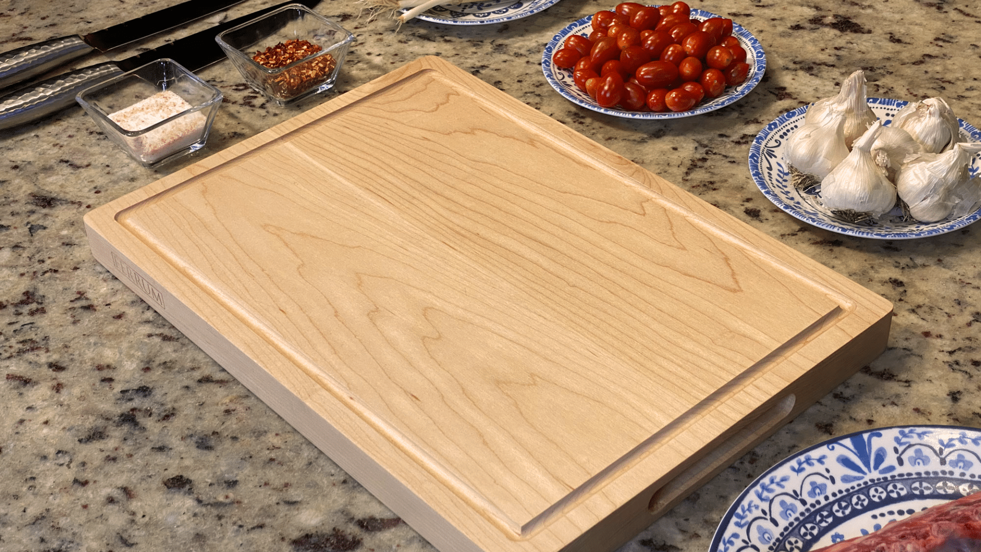 maple cutting board on a granite counter beside tomatoes, garlic, salt, and seasonings