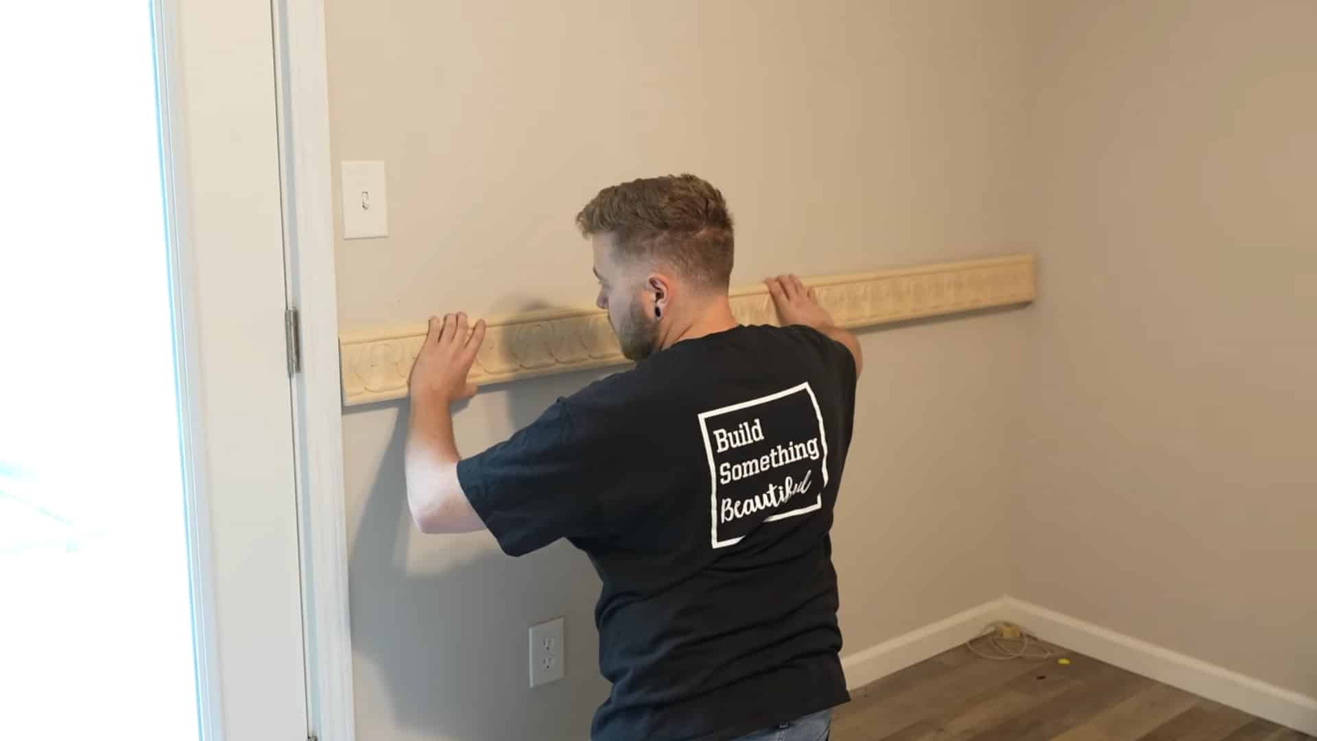 installer applying adhesive to wooden chair rail molding before mounting it on the wall