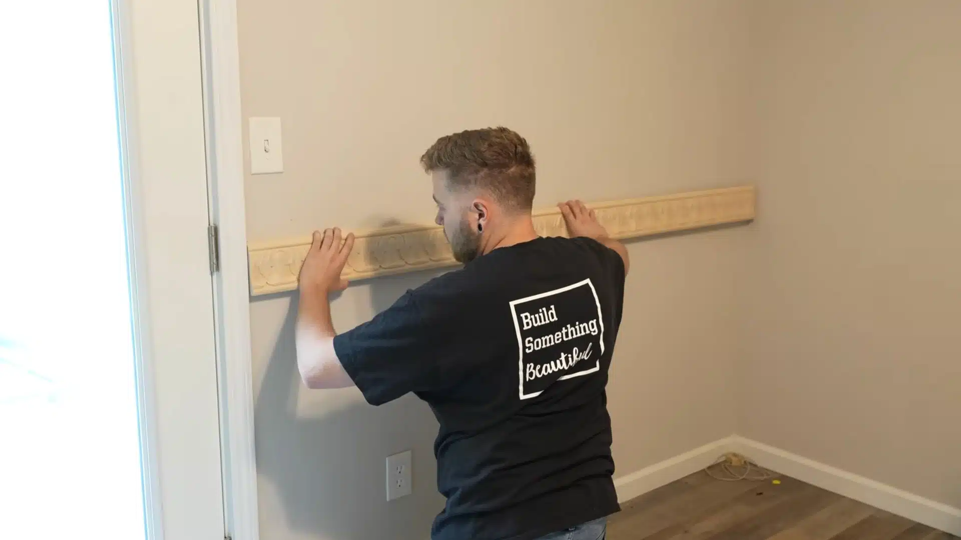 installer applying adhesive to wooden chair rail molding before mounting it on the wall