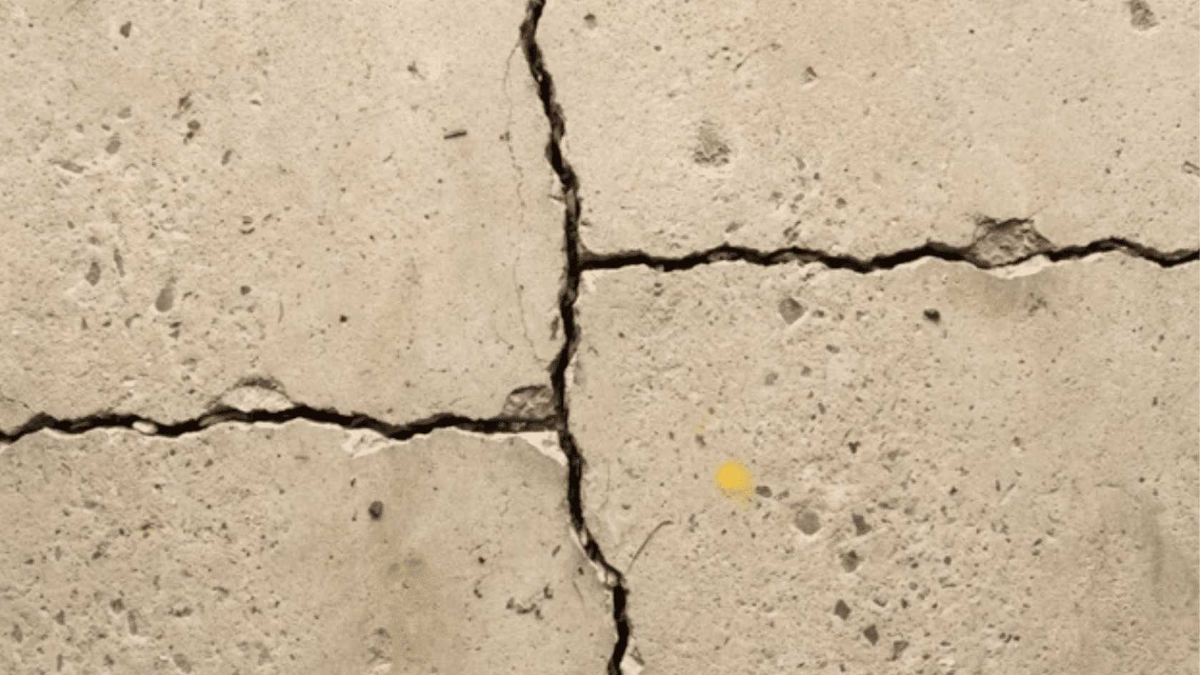 close-up of intersecting cracks in a weathered concrete slab with visible surface damage.