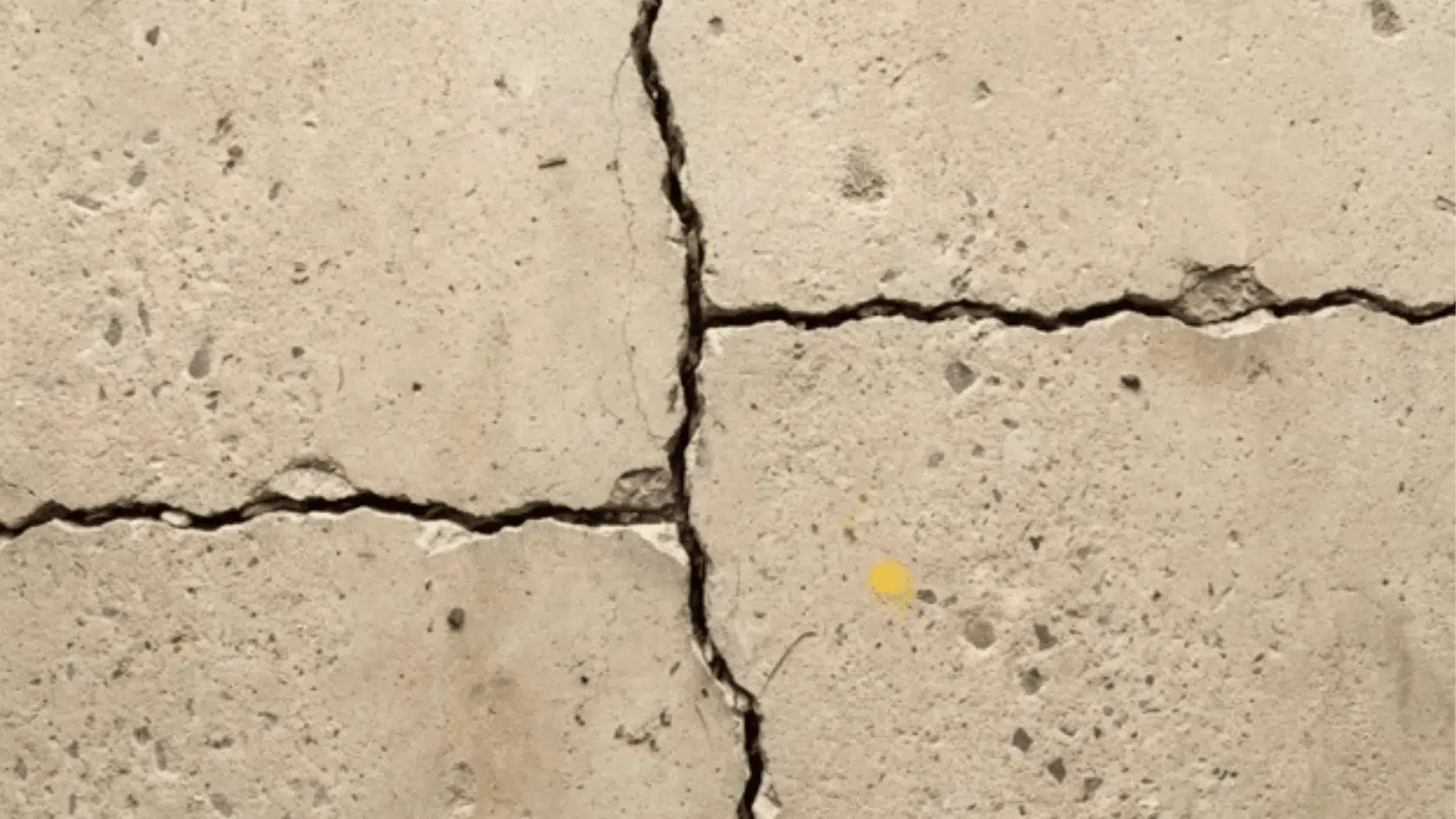 close-up of intersecting cracks in a weathered concrete slab with visible surface damage.