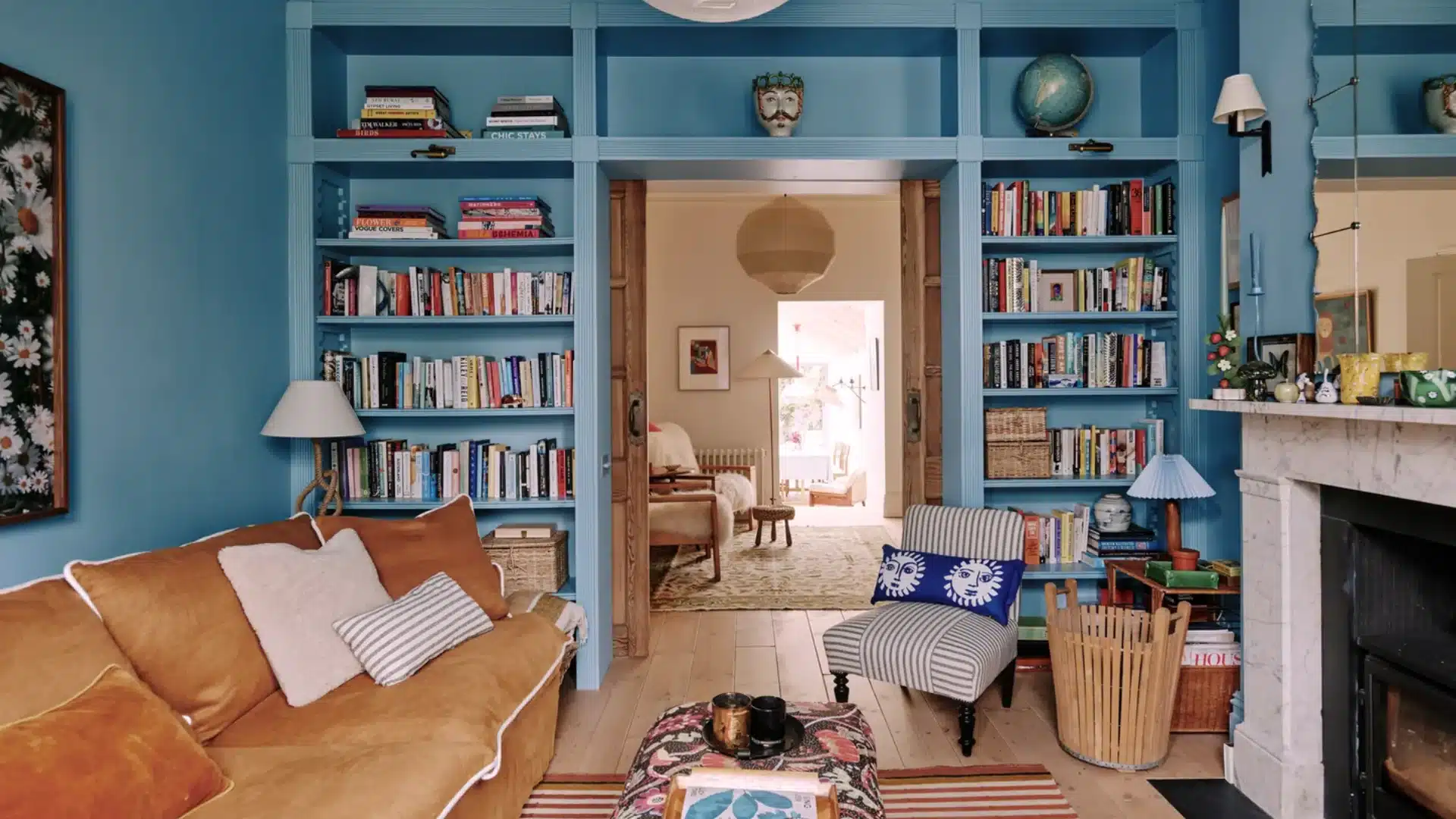 Cozy living room with blue built-in shelves, pocket doors, fireplace, and colorful seating with books and decor