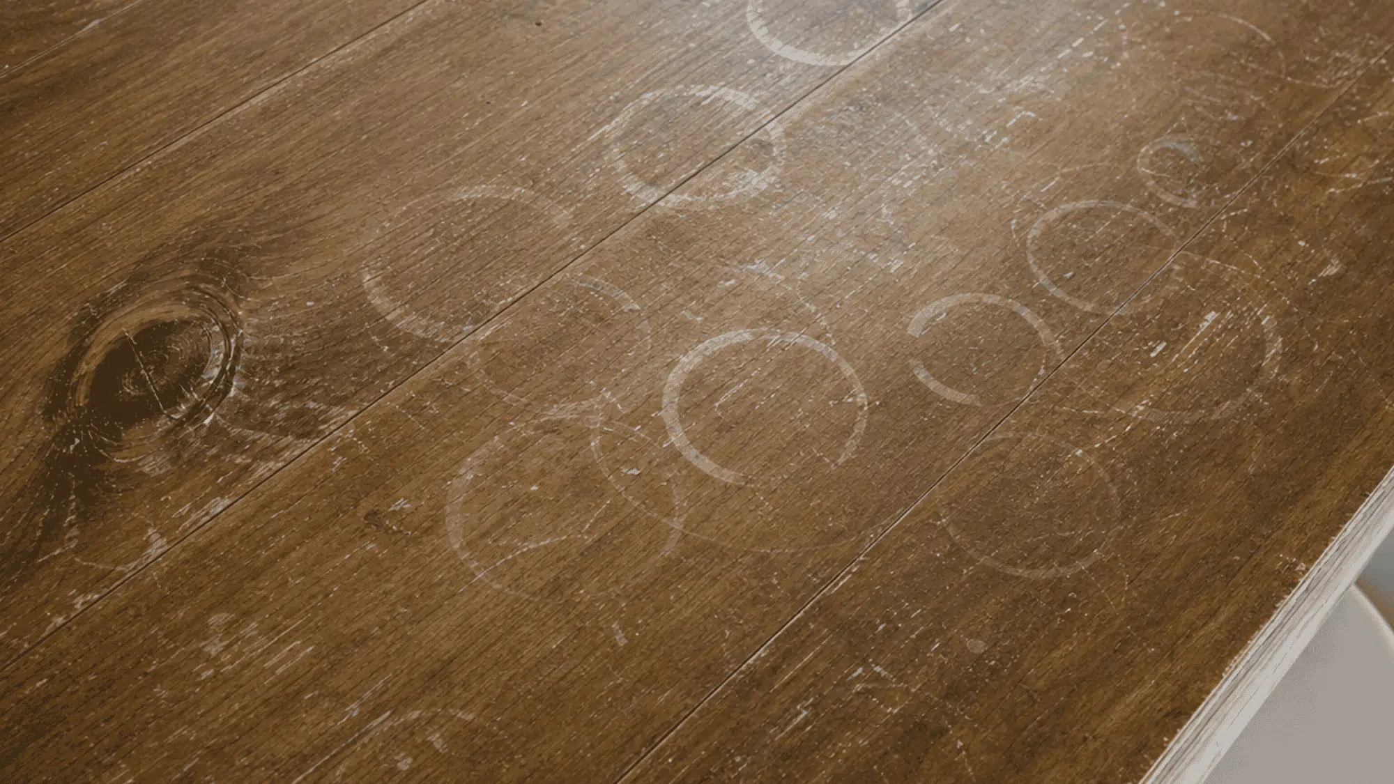 White water rings and stains visible across a dark wooden tabletop from cups and moisture damage