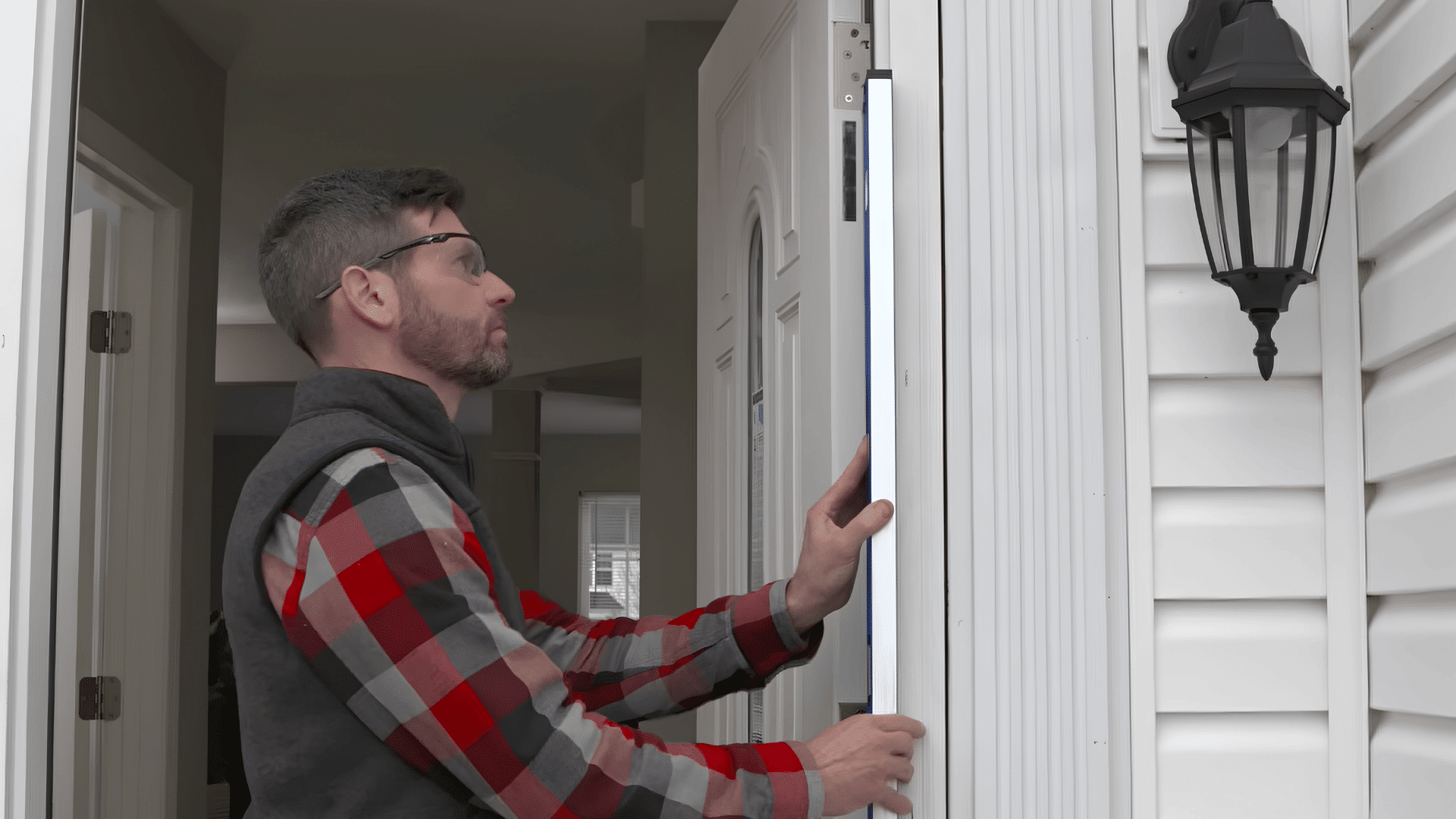 Worker checking a white exterior door frame with a long spirit level.