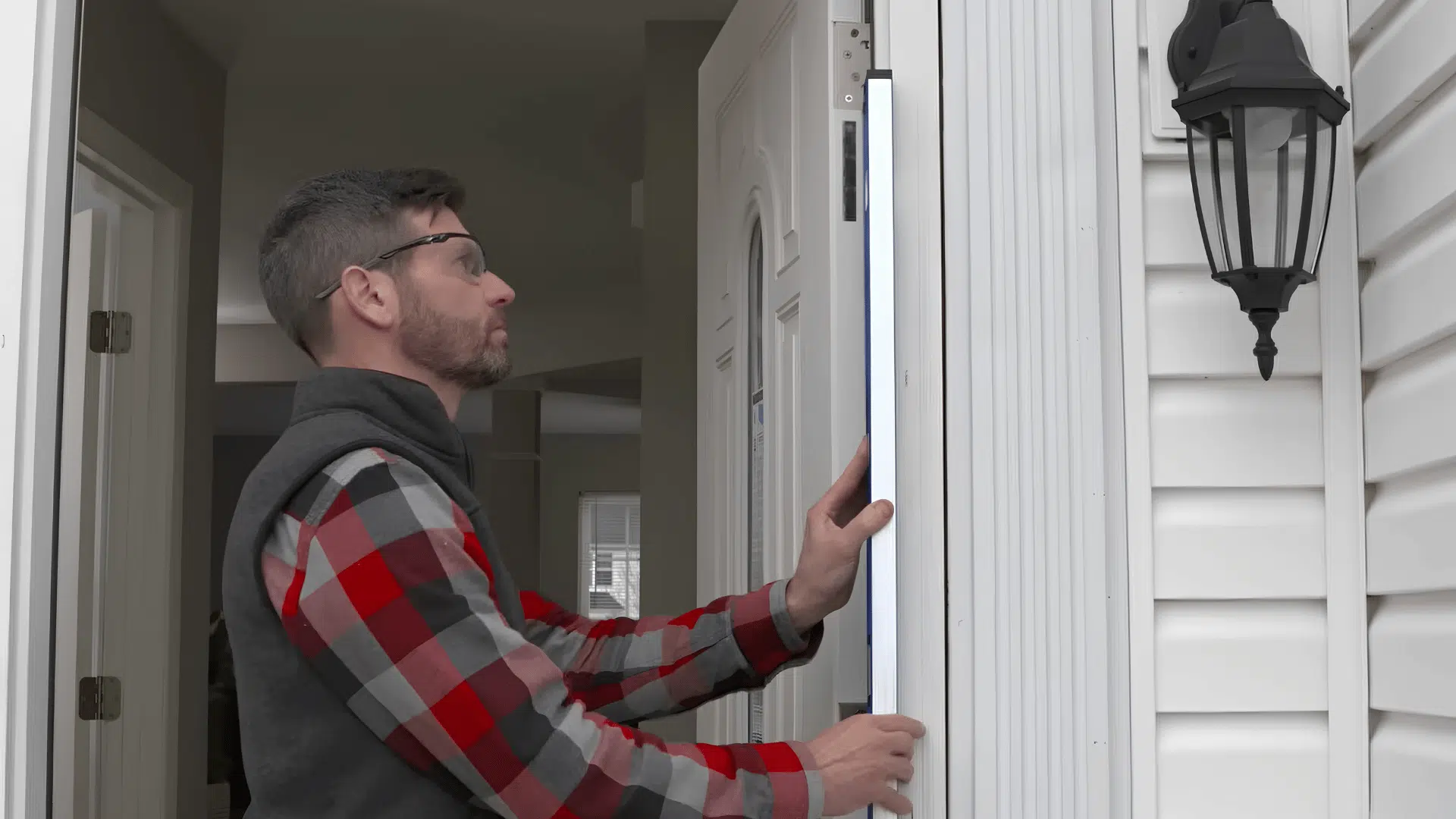 Worker checking a white exterior door frame with a long spirit level.