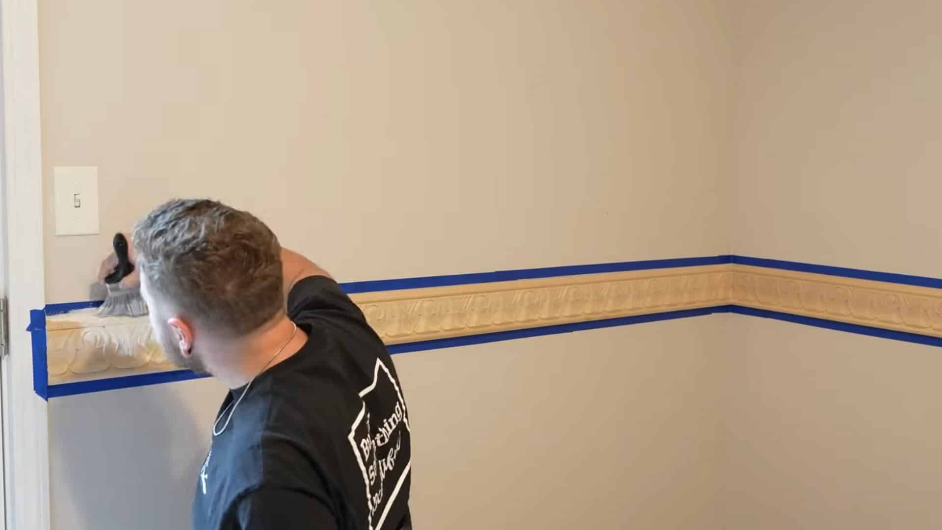 installer masking chair rail edges with blue tape before painting the wall