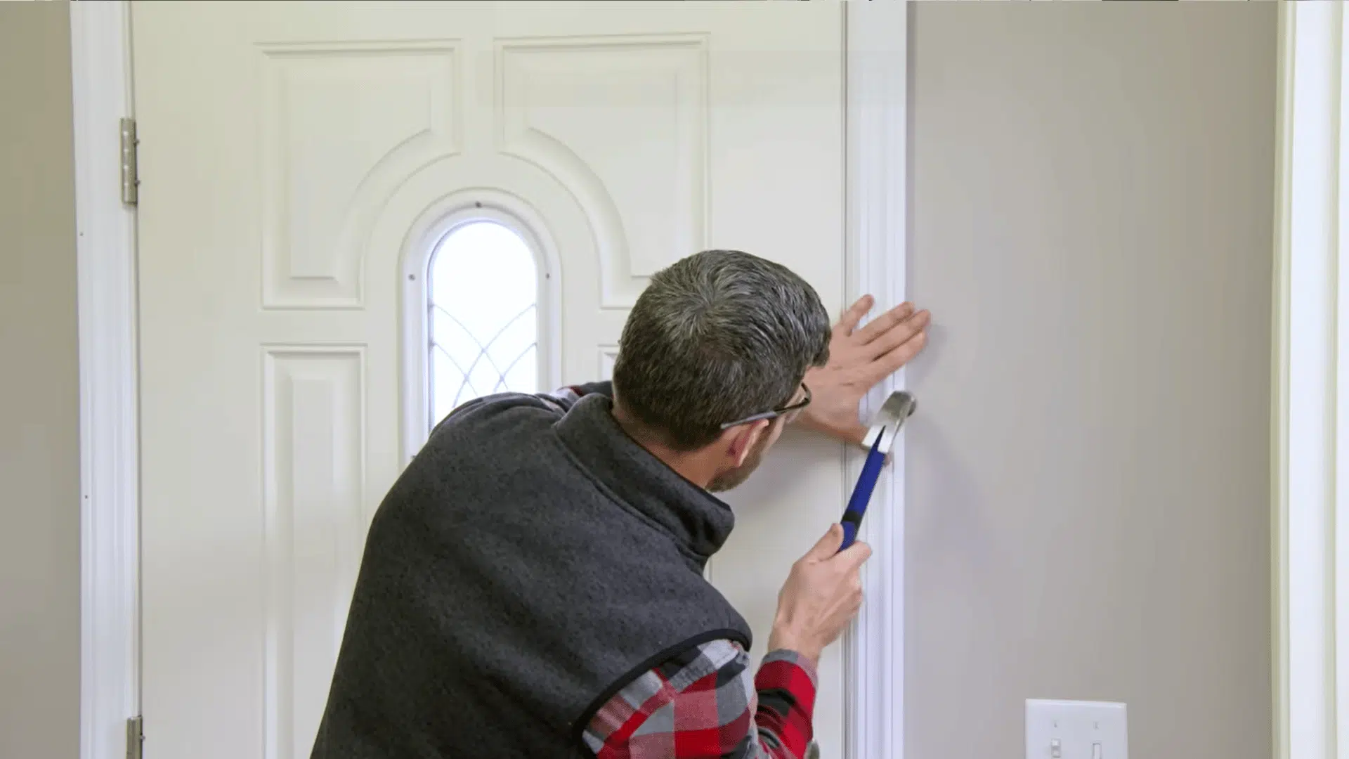Worker removing interior door trim with a pry bar during prehung door replacement.
