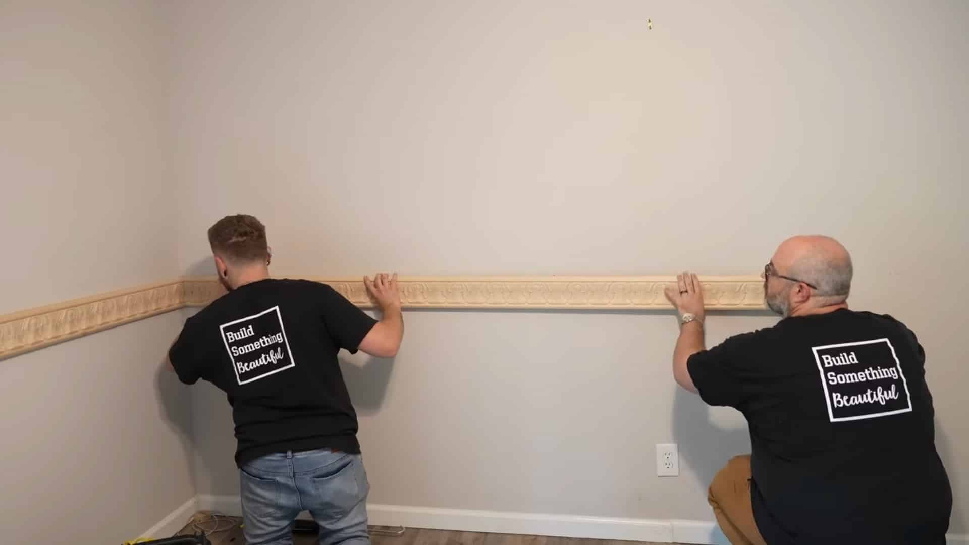 two installers securing wooden chair rail molding to the wall with finish nails