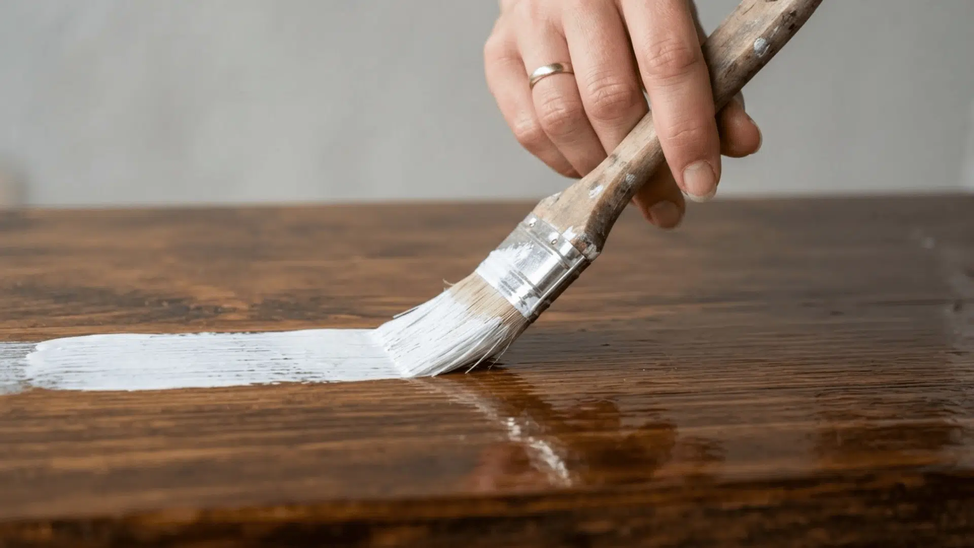 Hand applying white paint over a polyurethane-coated wooden surface.