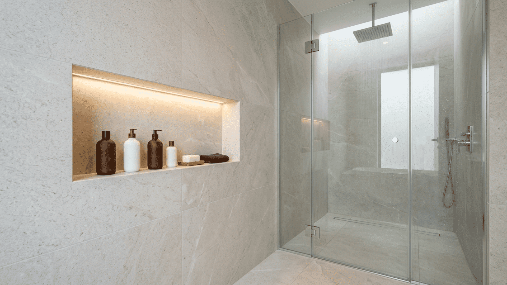 tiled shower with a lit wall niche, glass enclosure, rainfall head, and bottles.