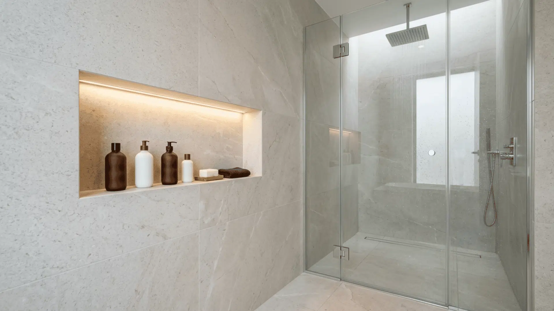 tiled shower with a lit wall niche, glass enclosure, rainfall head, and bottles.