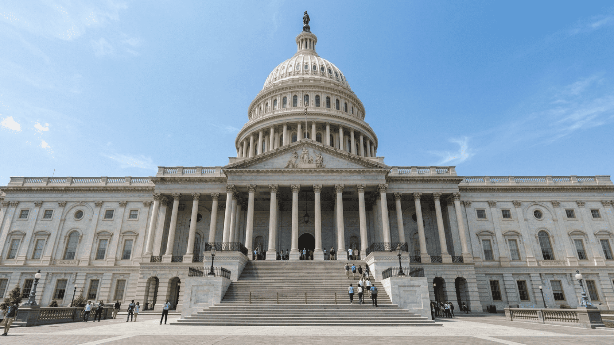 US Capitol building featuring a grand dome, Classical columns, and broad stone steps beneath blue sky.