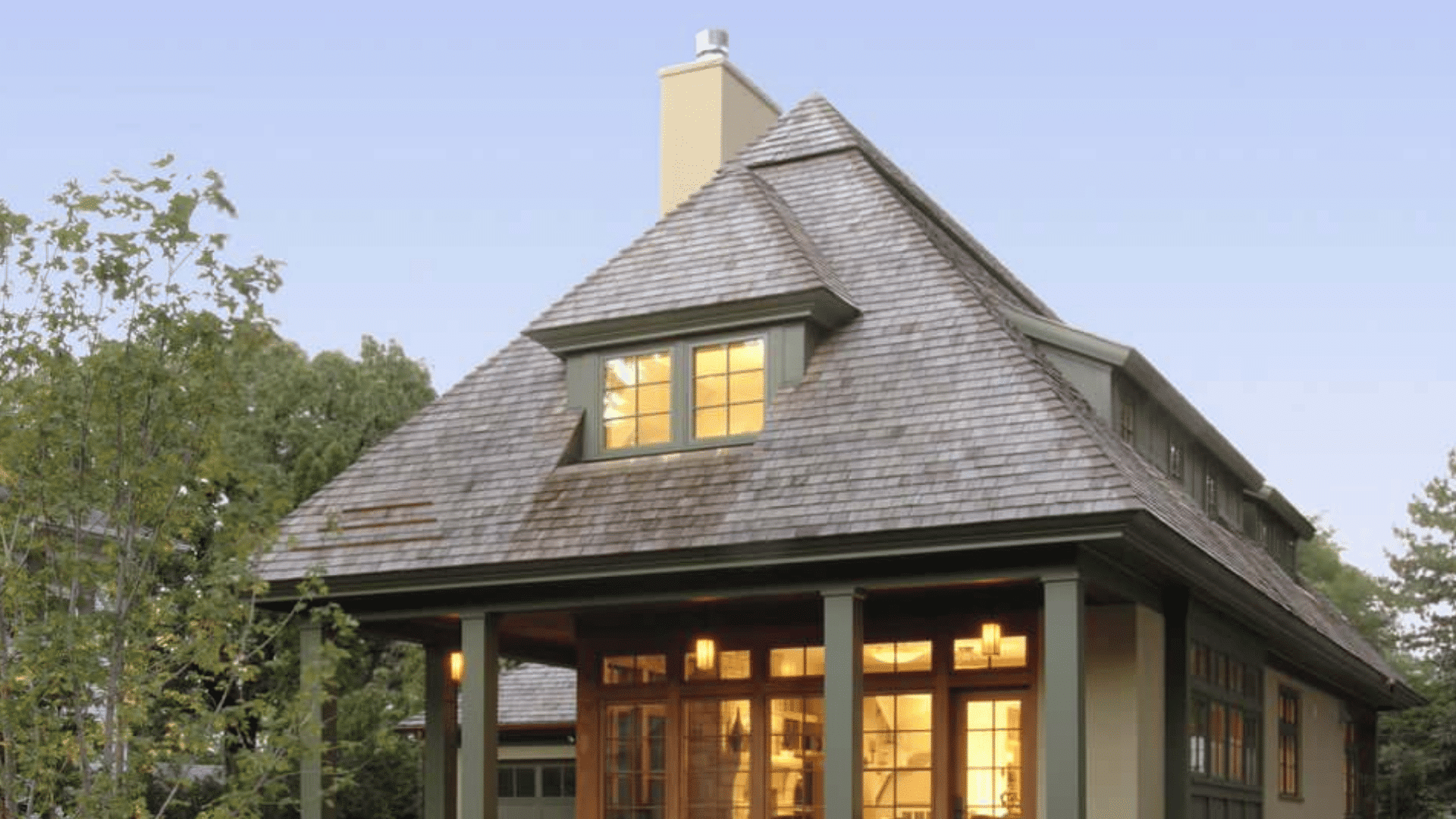 hipped dormer with illuminated windows set into a broad shingled roof at dusk