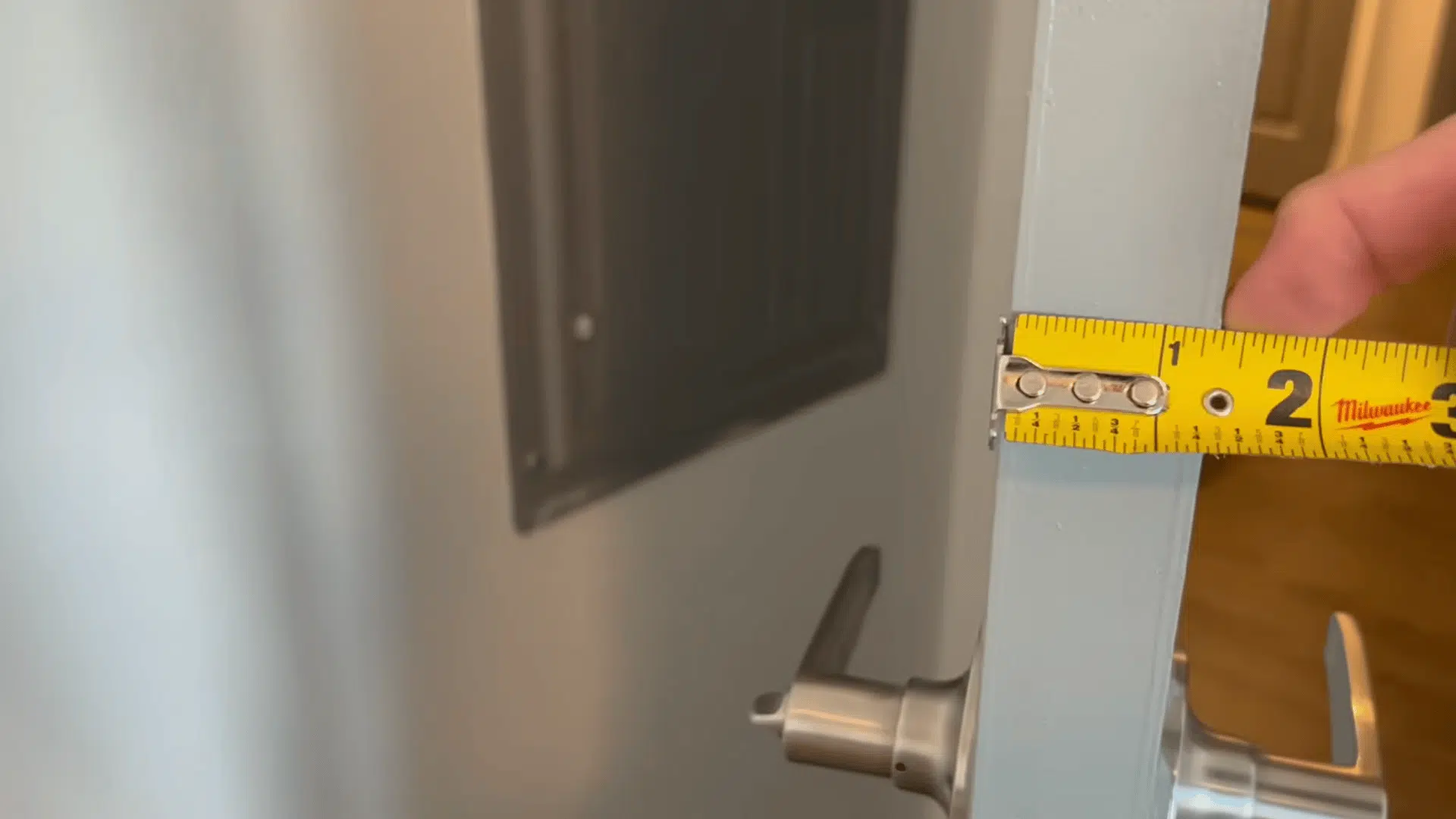 close-up of a tape measure measuring an interior door's thickness for door replacement.