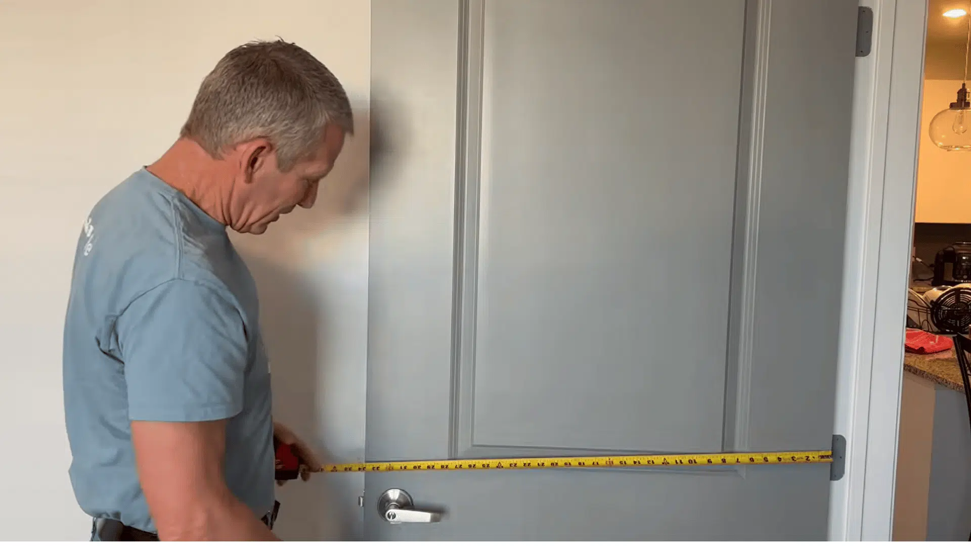 Man measuring the width of an interior door horizontally with a tape measure.