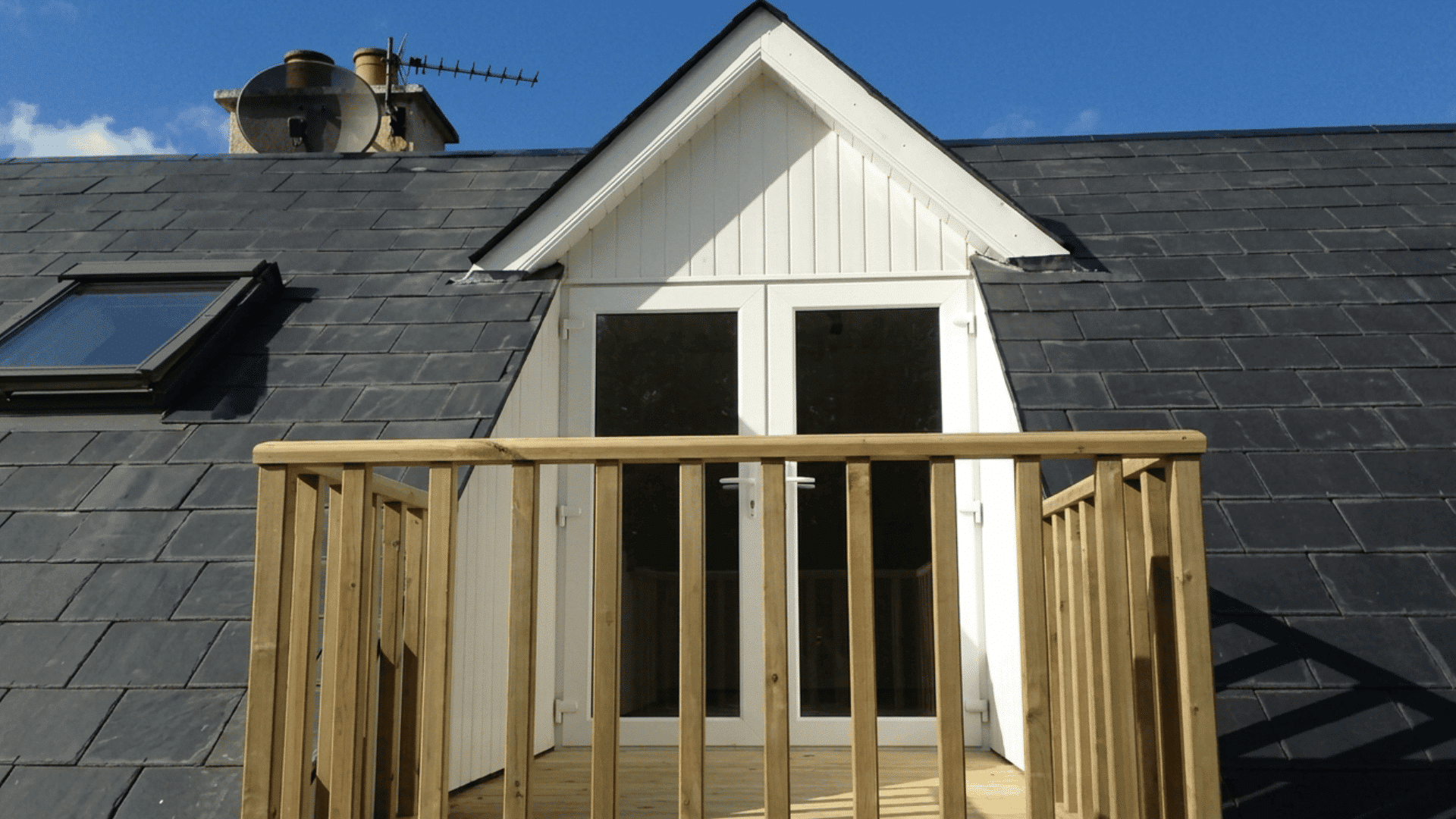 recessed gable dormer with glass doors opening onto a small wooden balcony
